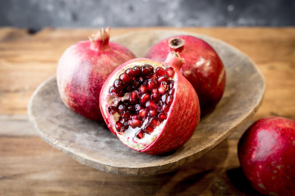 Three pomegranates on a rustic wooden plate, one slightly opened to reveal its seeds