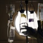 The nurse checks the IV fluids hanging from the poles next to the patient's bed.