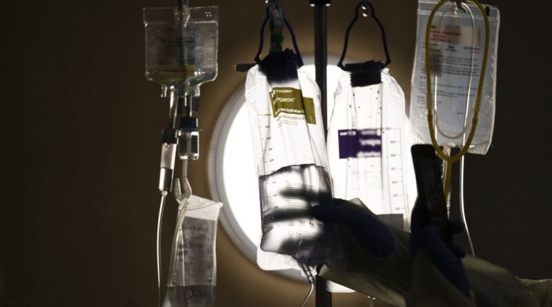 The nurse checks the IV fluids hanging from the poles next to the patient's bed.