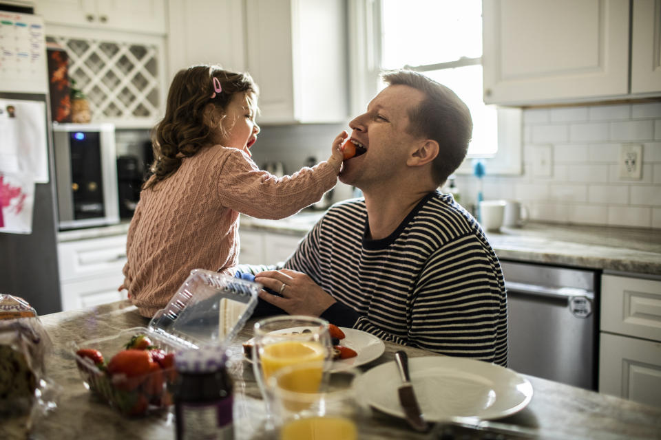 A girl feeds her father a strawberry in the kitchen