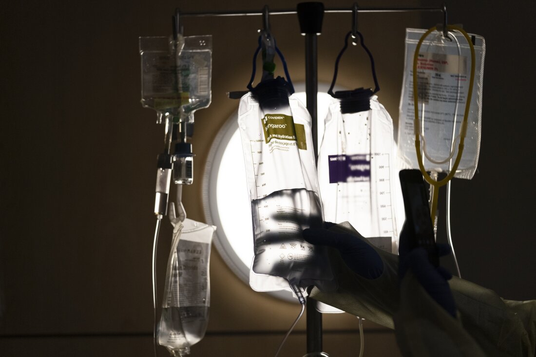 The nurse checks the IV fluids hanging from the poles next to the patient's bed.