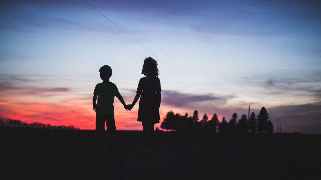 silhouettes of two children against the dusk sky